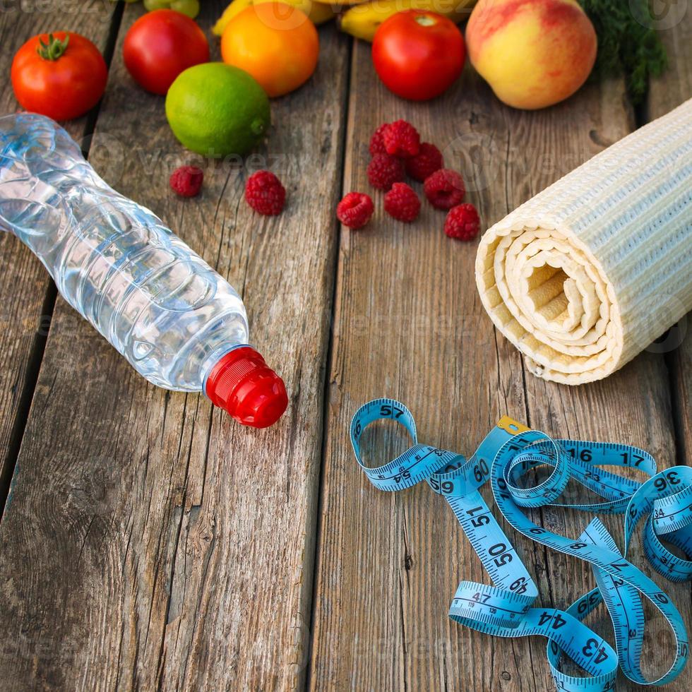 Fruits, vegetables, water, measurement tape and sports goods on wooden background. photo