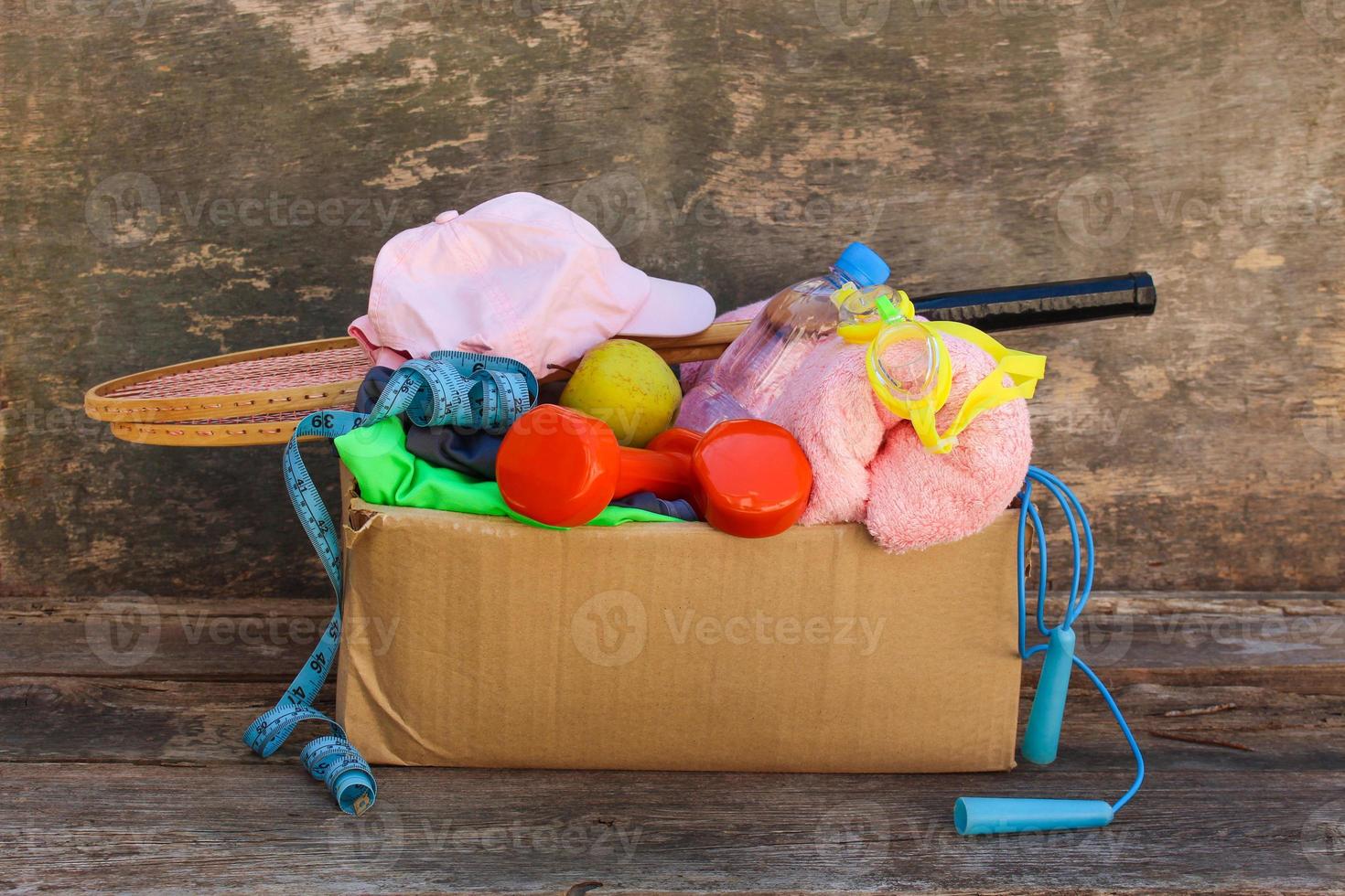 Cardboard box with sports stuff on old wooden background. photo