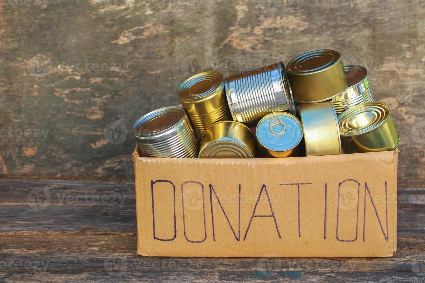 Donation box with different canned food on old wooden background. photo