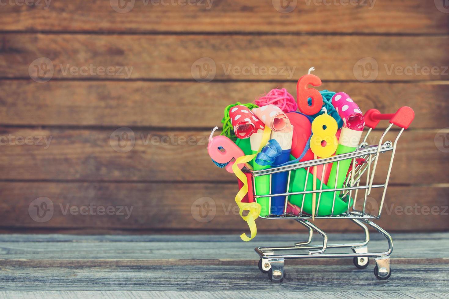 Shopping cart with items for birthday celebration on wooden background. Toned image. photo