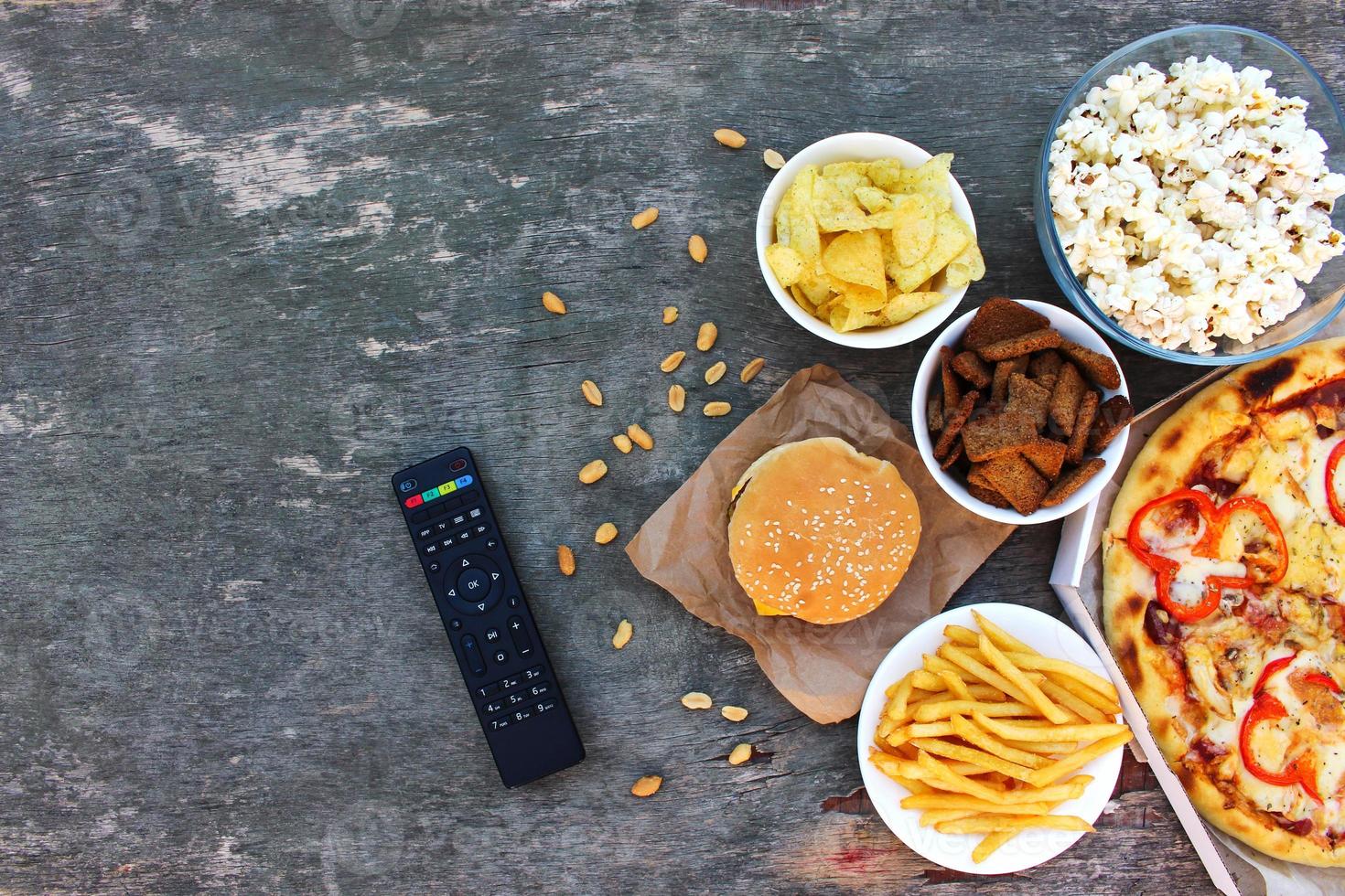 TV remote control, fast food on old wooden background. Concept of junk eating. Top view. Flat lay. photo
