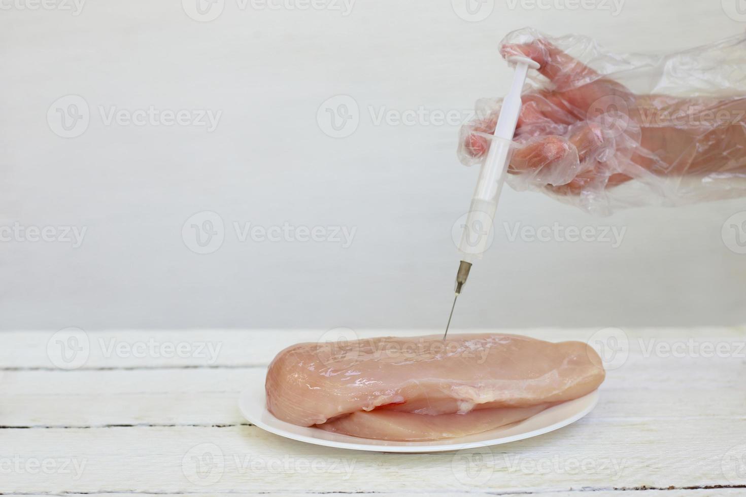 People make injection syringe in chicken fillet on white background. photo
