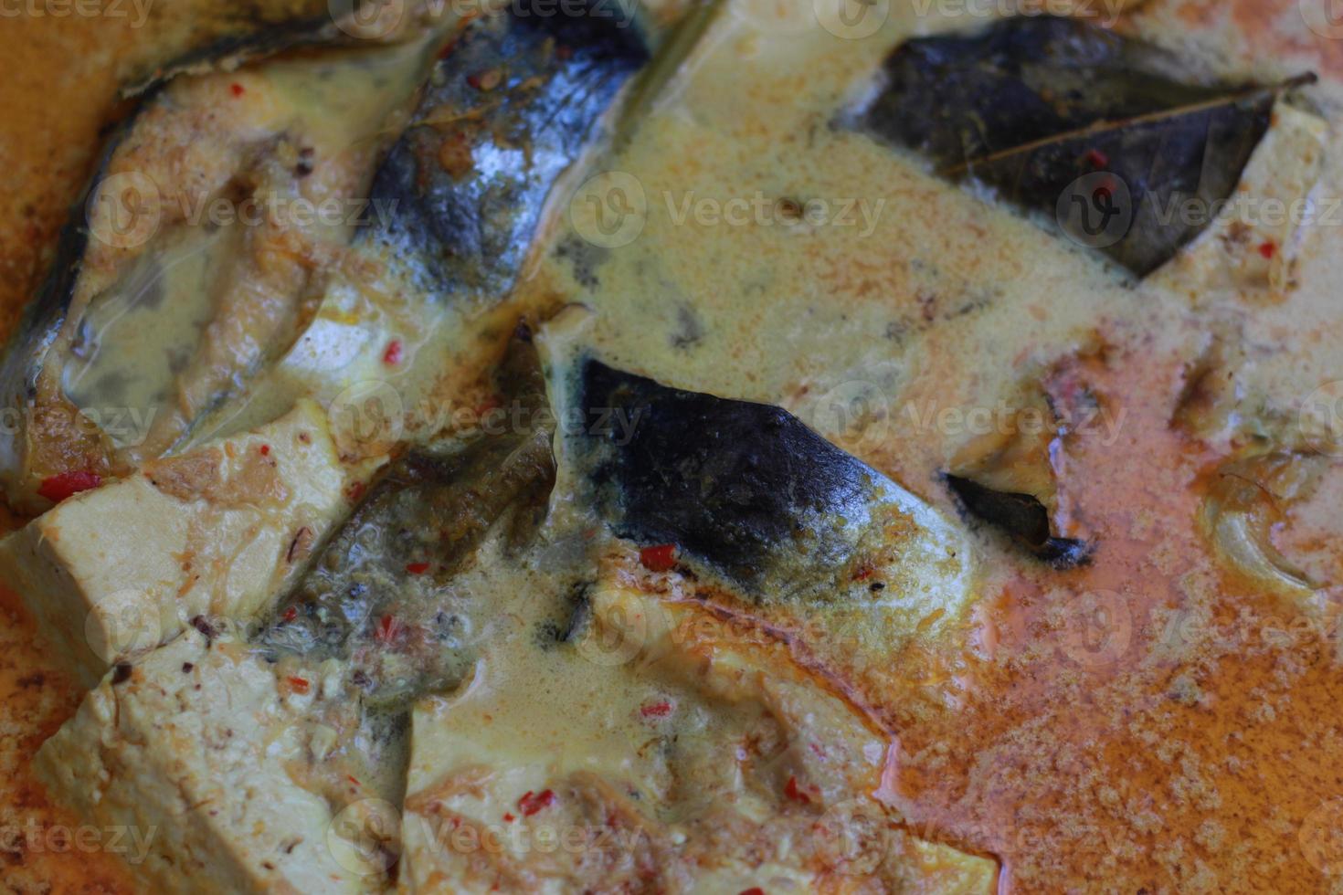 photo of tuna fish and white tofu in yellow spice sauce on a frying pan. Indonesian traditional food photo concept.