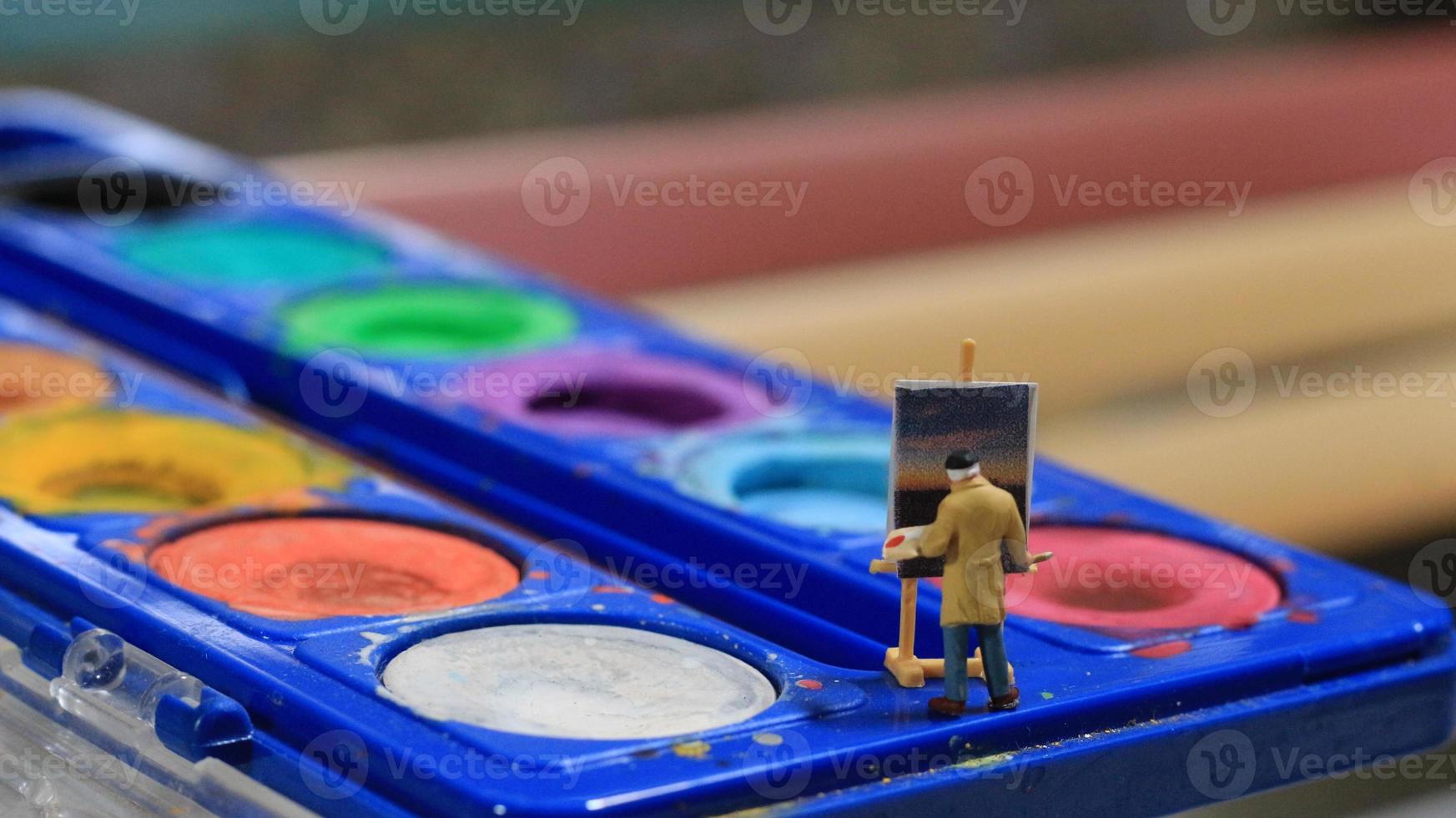 a miniature figure of a painter painting a landscape on watercolors. artist concept. photo