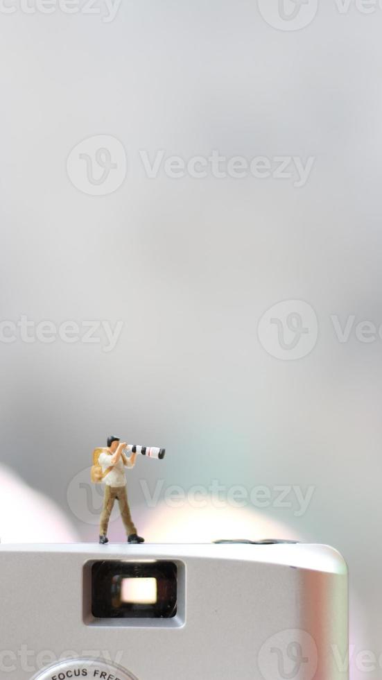 a miniature figure taking picture with a camera against a real camera in the background. photo