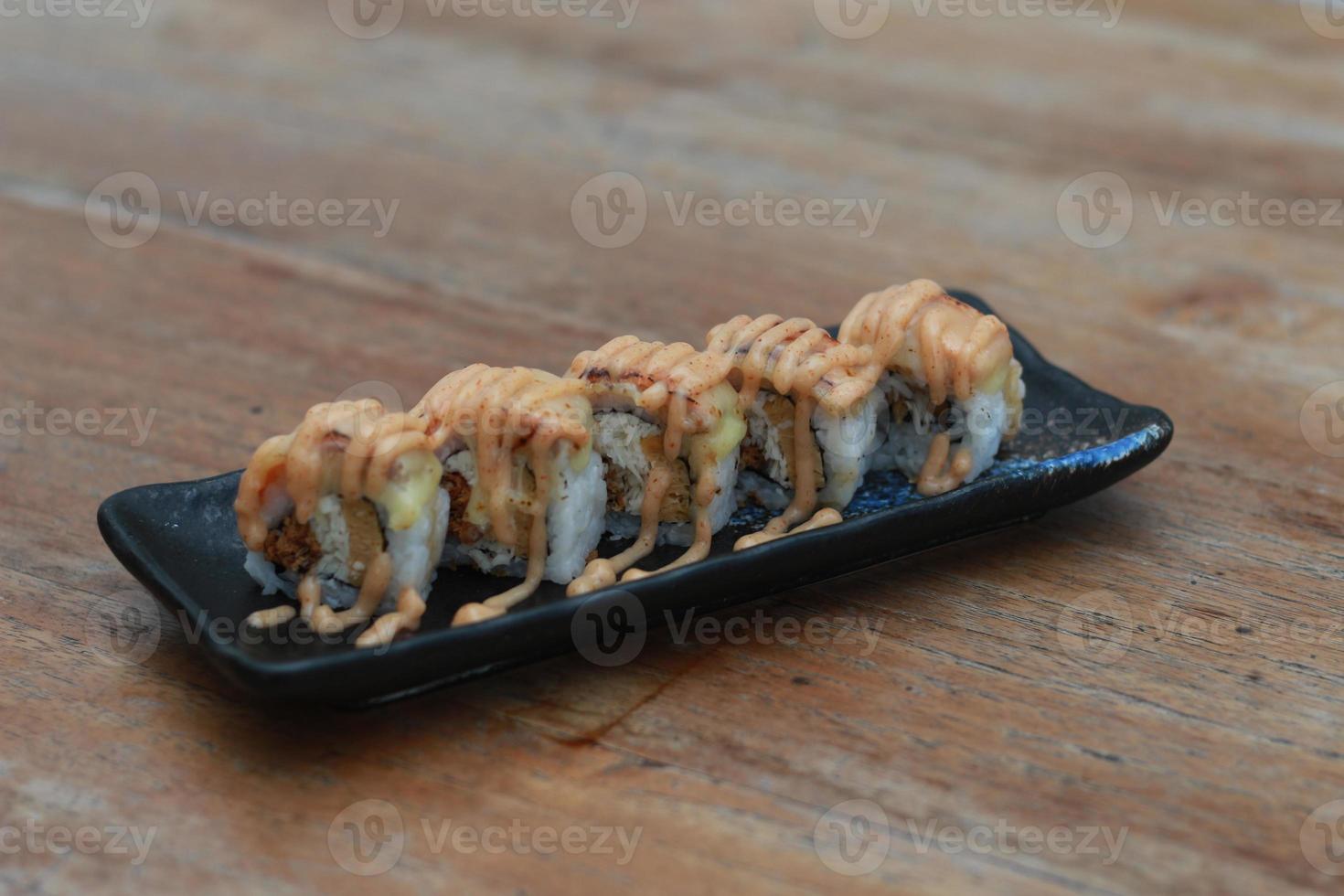 Japanese food called Salmon Mozza Sushi. Served warm on a black rectangular plate on the table. photo