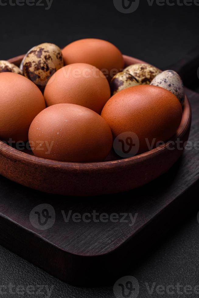 Raw chicken and quail eggs in a brown ceramic bowl on a dark concrete background photo