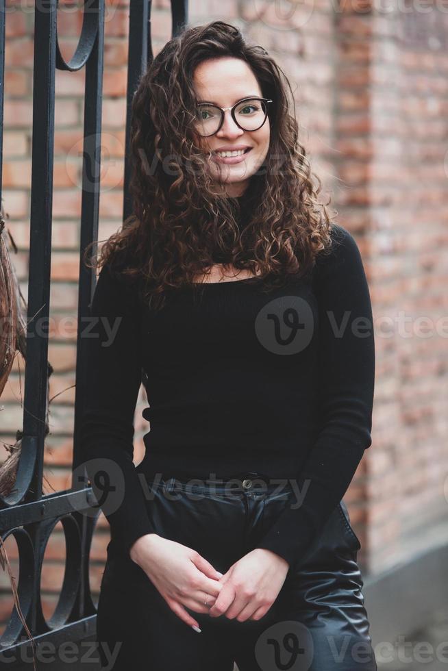 hermosa joven mujer con morena Rizado cabello, retrato en ojo lentes disfrutando el Dom en el ciudad. foto