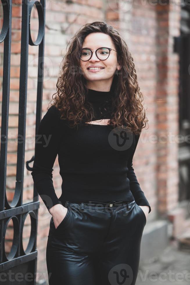 Beautiful young woman with brunette curly hair, portrait in eye glasses enjoying the sun in the city. photo