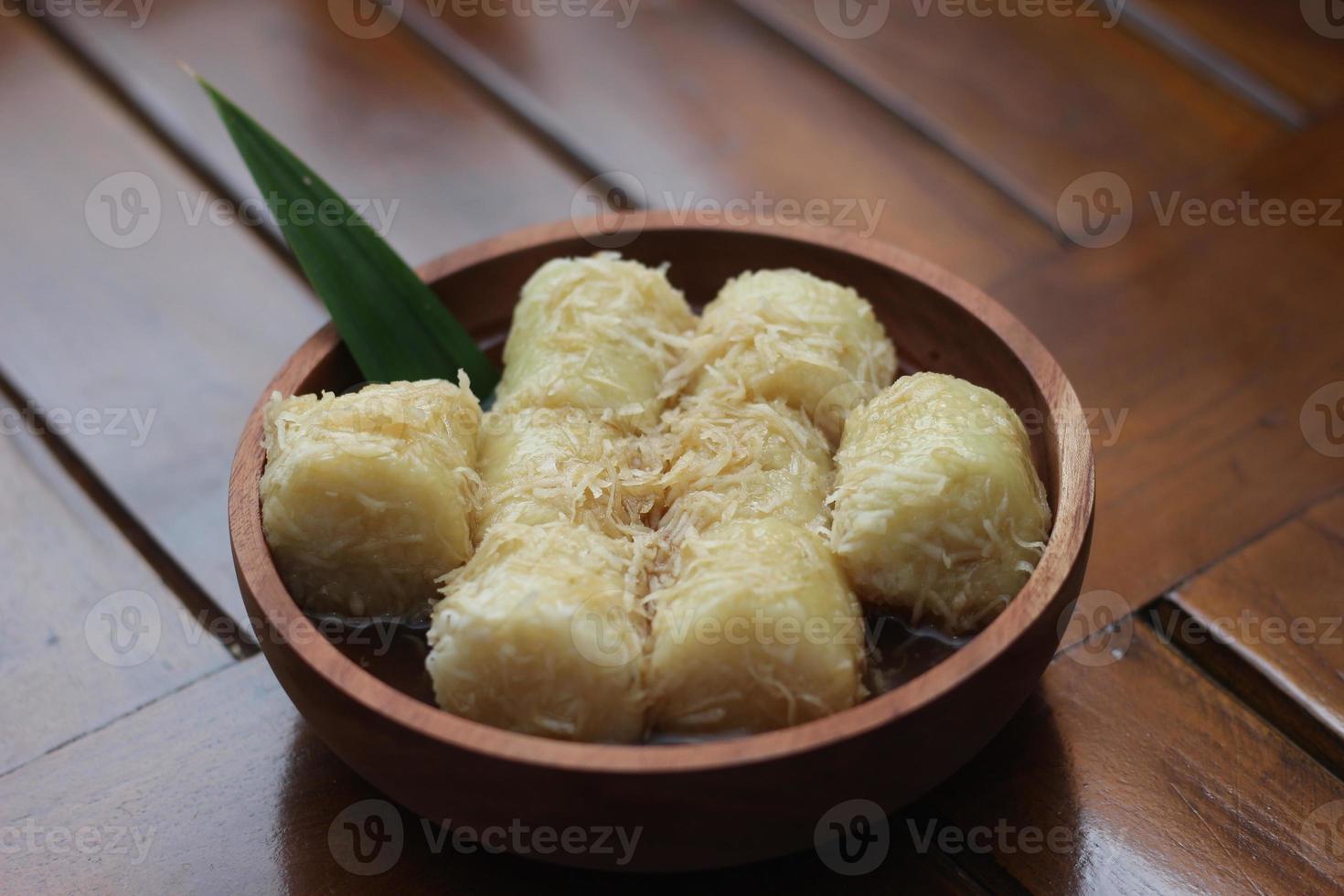 a close up of lupis with grated coconut and brown sugar sauce served in a wooden bowl. Indonesian traditional food photo concept.