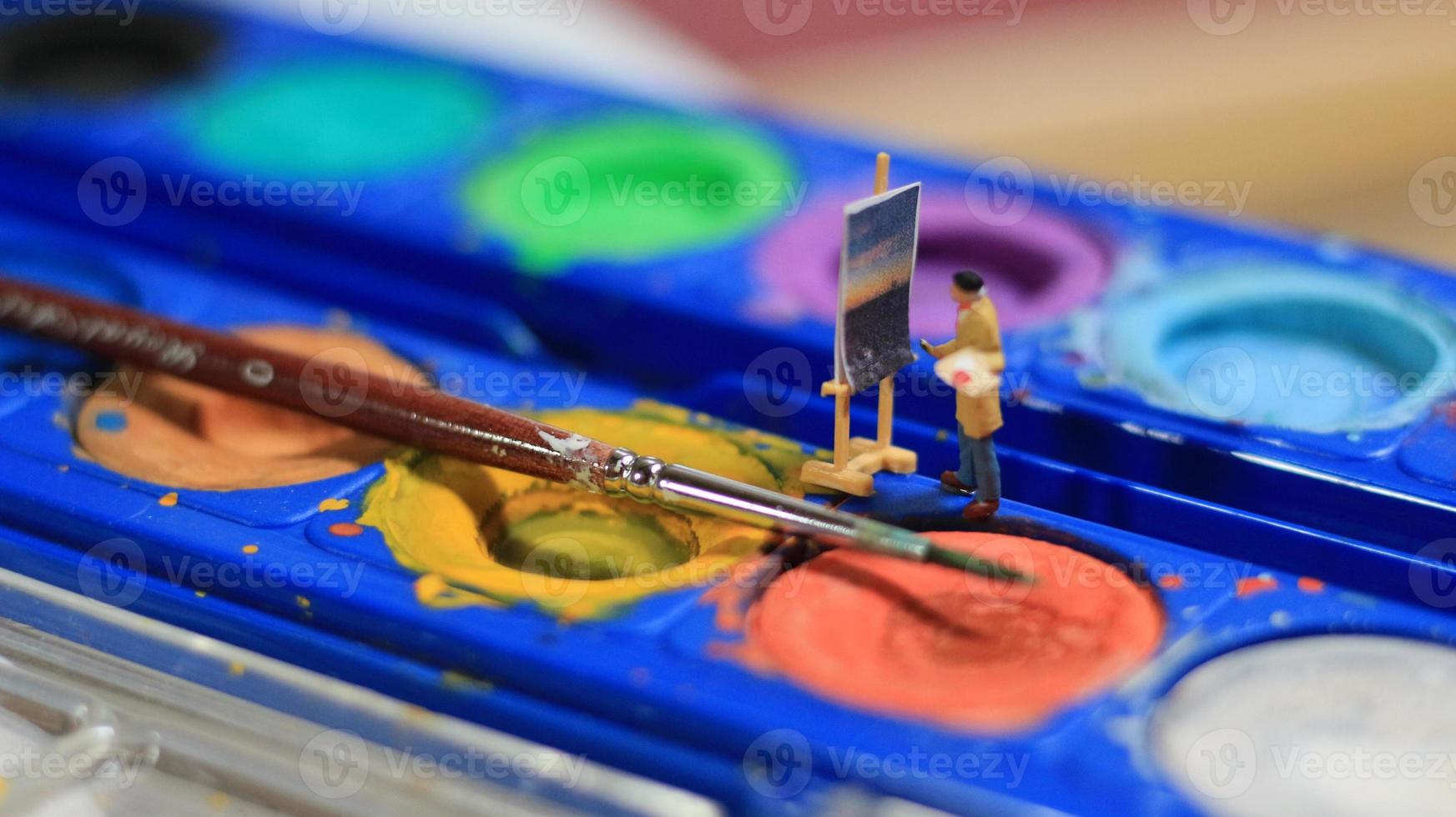a miniature figure of a painter painting a landscape on watercolors. artist concept. photo