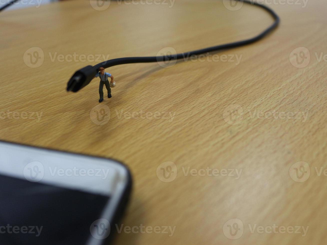 a miniature figure of a worker carrying a cellphone charging cable. photo