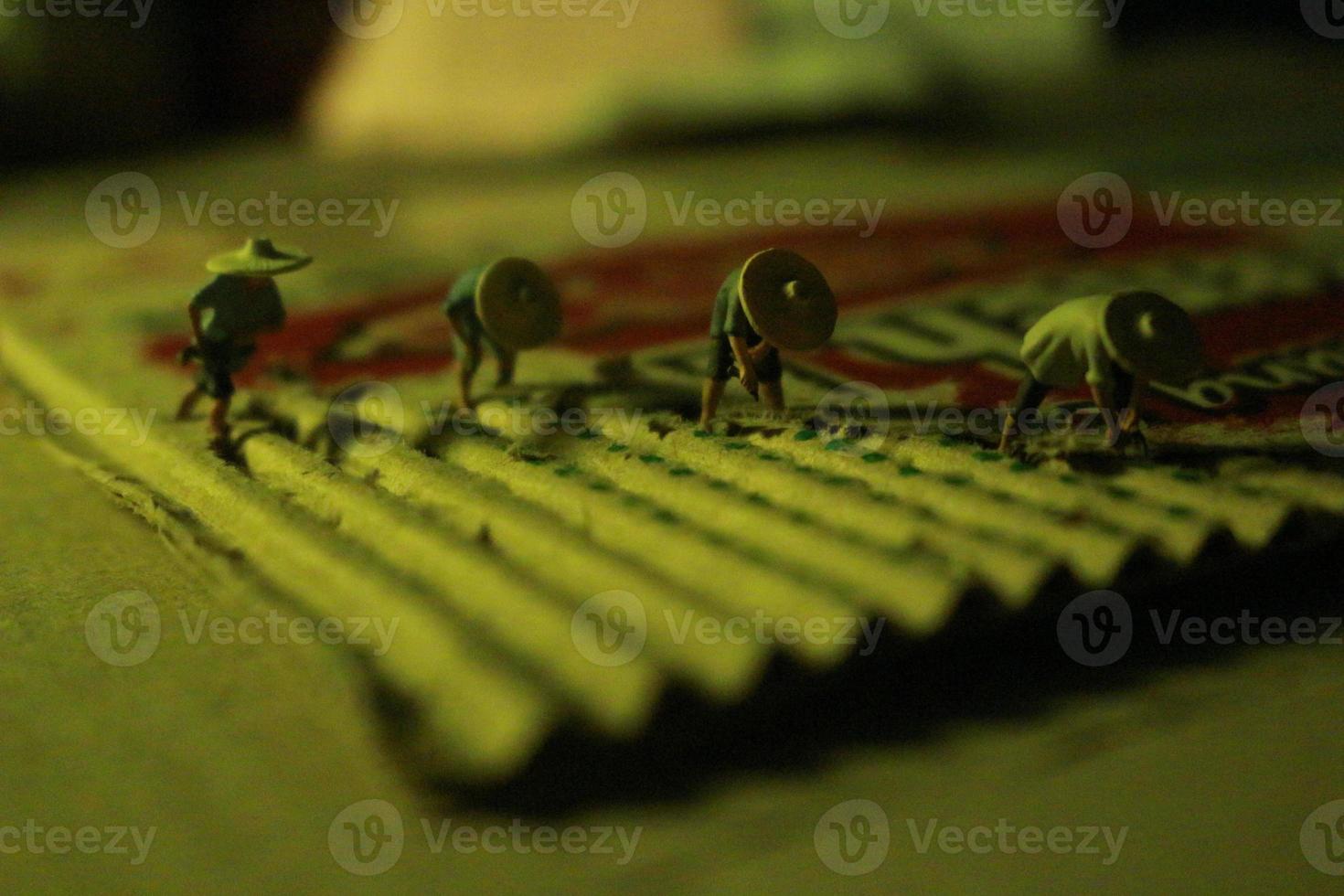 a close up of miniature figures of farmers who are farming on cardboard pieces like rice fields. farmer farming concept. photo