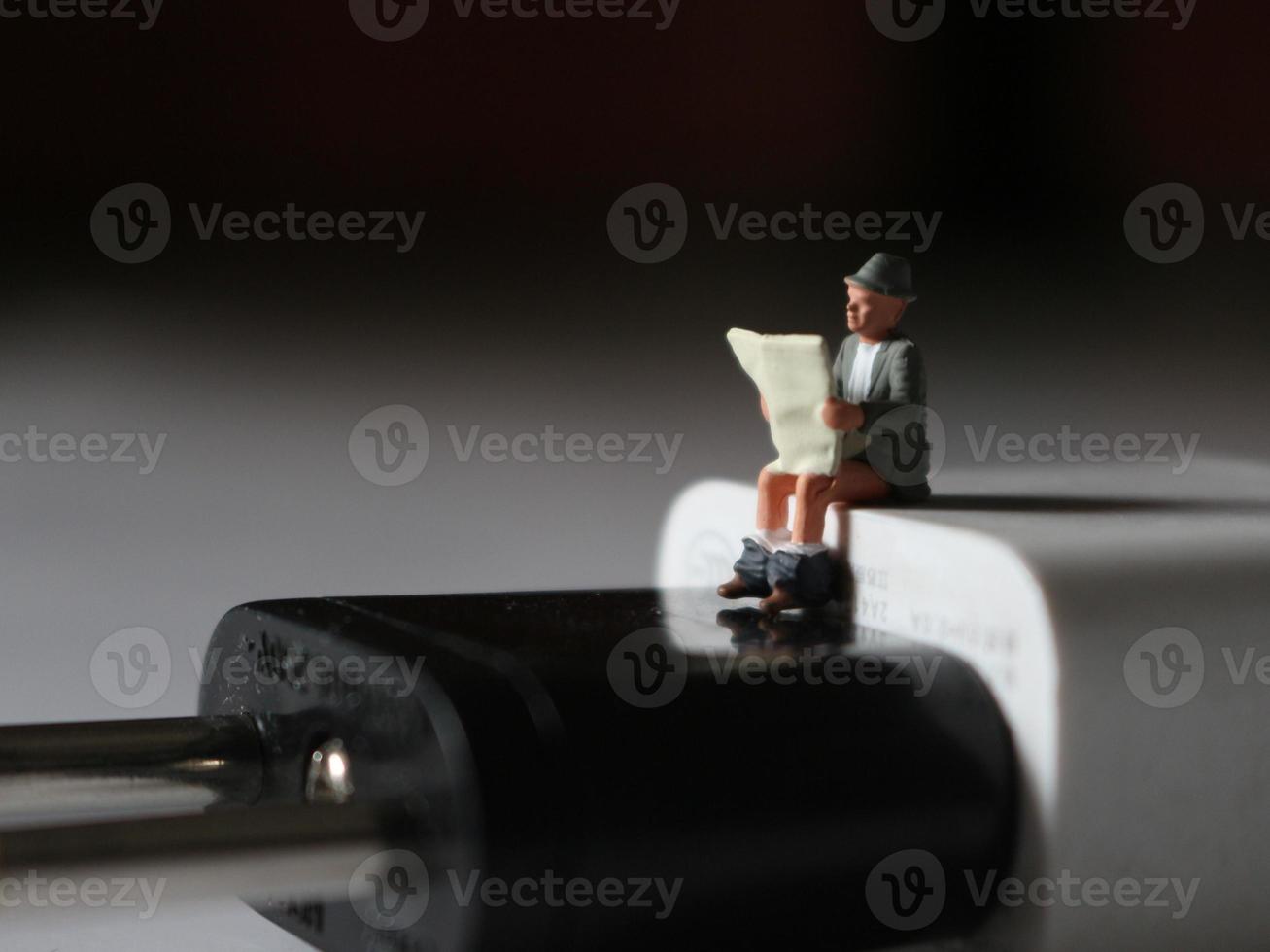 a close up of a miniature figure of a person reading above a cell phone charger. photo