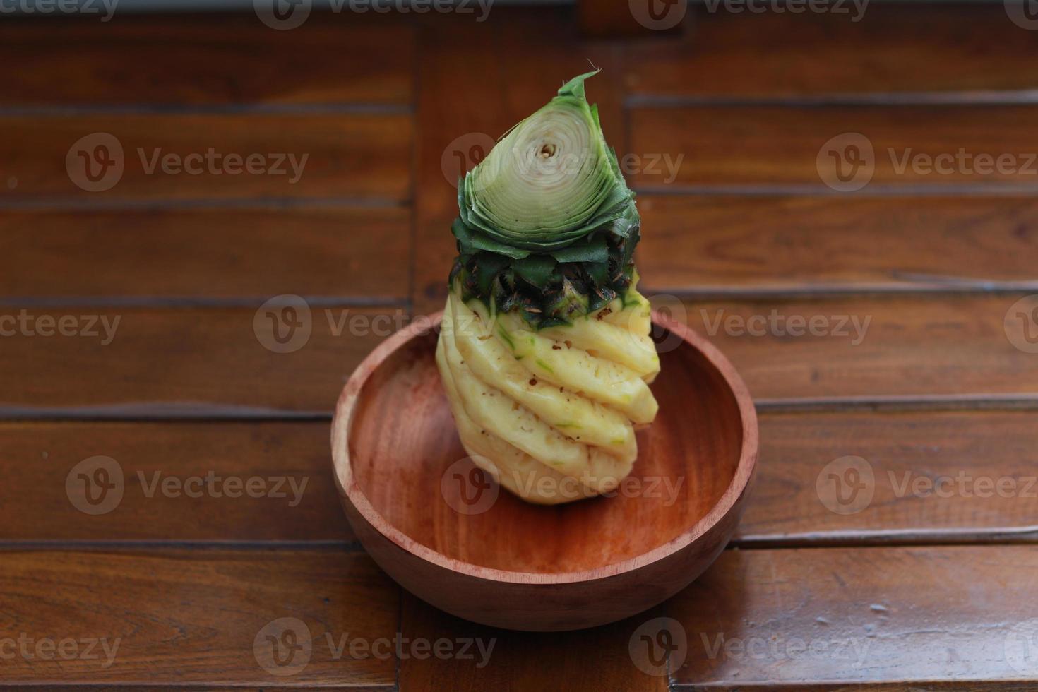 a close up of a peeled pineapple on a wooden bowl. fruit photo concept.