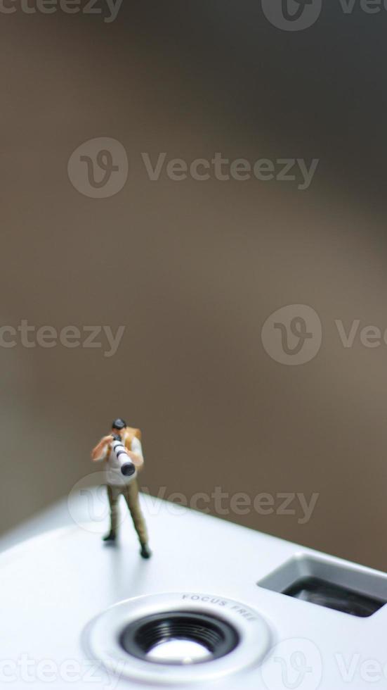 un miniatura figura tomando imagen con un cámara en contra un real cámara en el antecedentes. foto