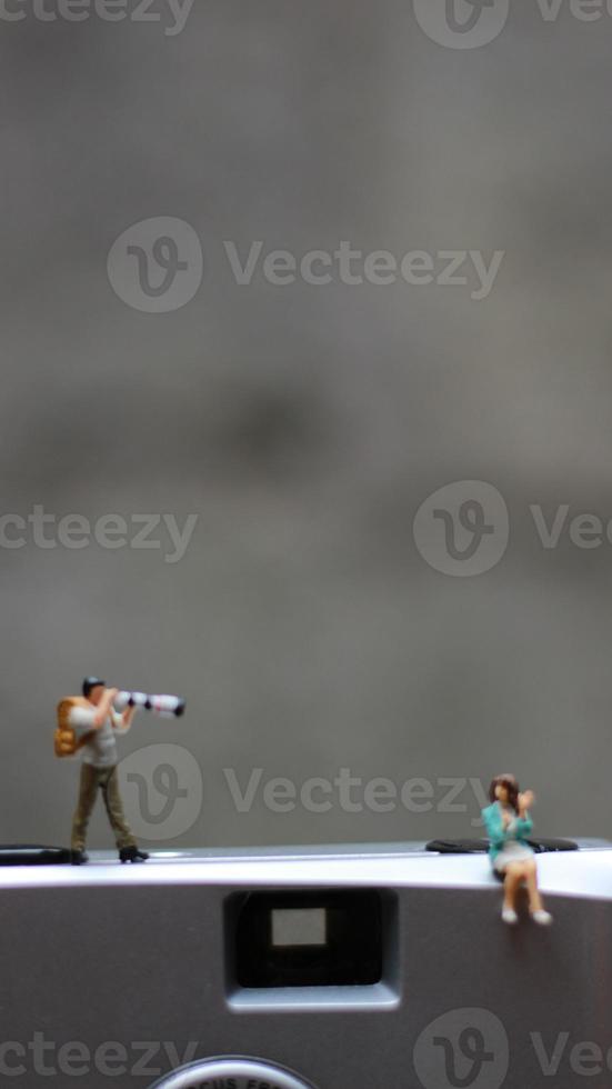 a miniature figure taking picture with a camera against a real camera in the background. photo