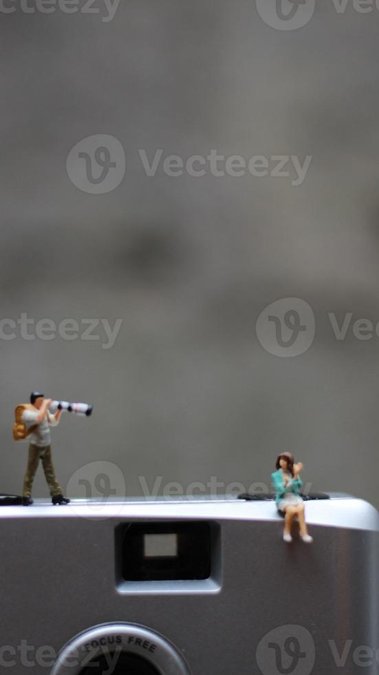 a miniature figure taking picture with a camera against a real camera in the background. photo