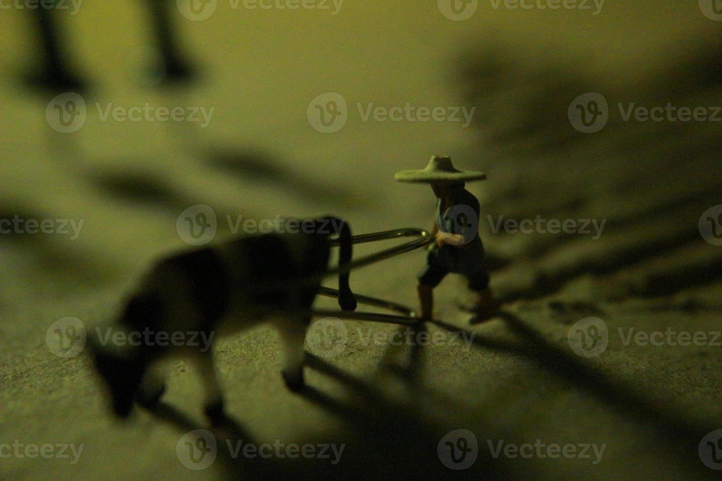 miniature figure of a farmer plowing a field with his cow on a cardboard. photo