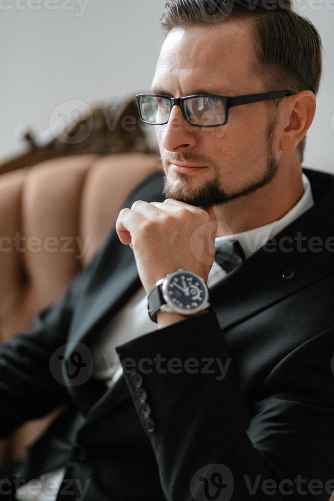 portrait of a groom in a black suit and glasses in a studio photo