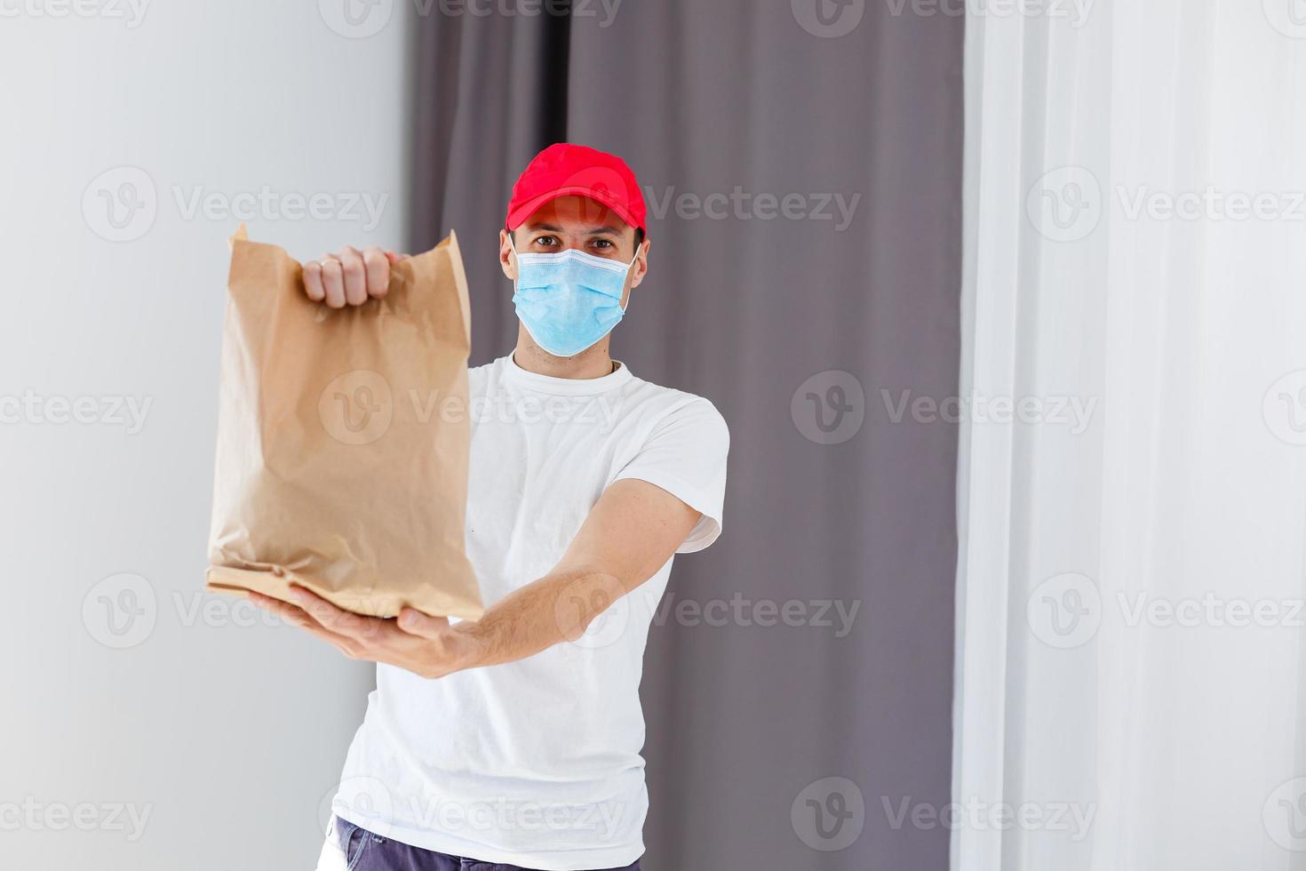 entrega hombre participación papel bolso con comida en blanco fondo, comida entrega hombre en protector máscara foto