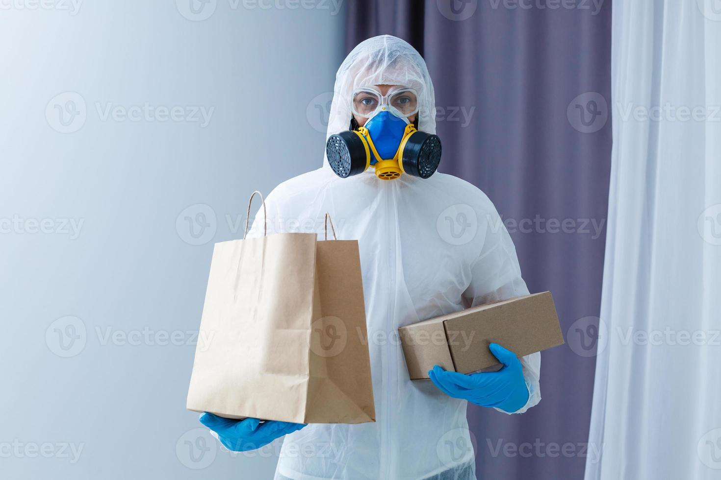 Man wearing chemical protective suit with cardboard box on light grey background. Coronavirus outbreak photo