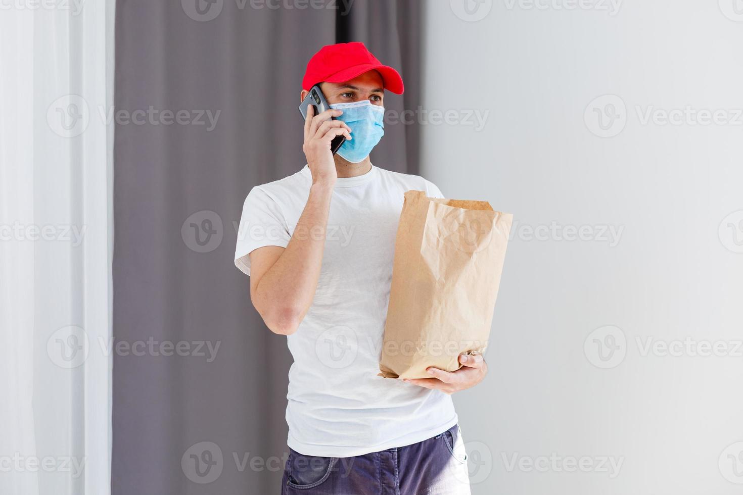 entrega hombre participación papel bolso con comida en blanco fondo, comida entrega hombre en protector máscara foto