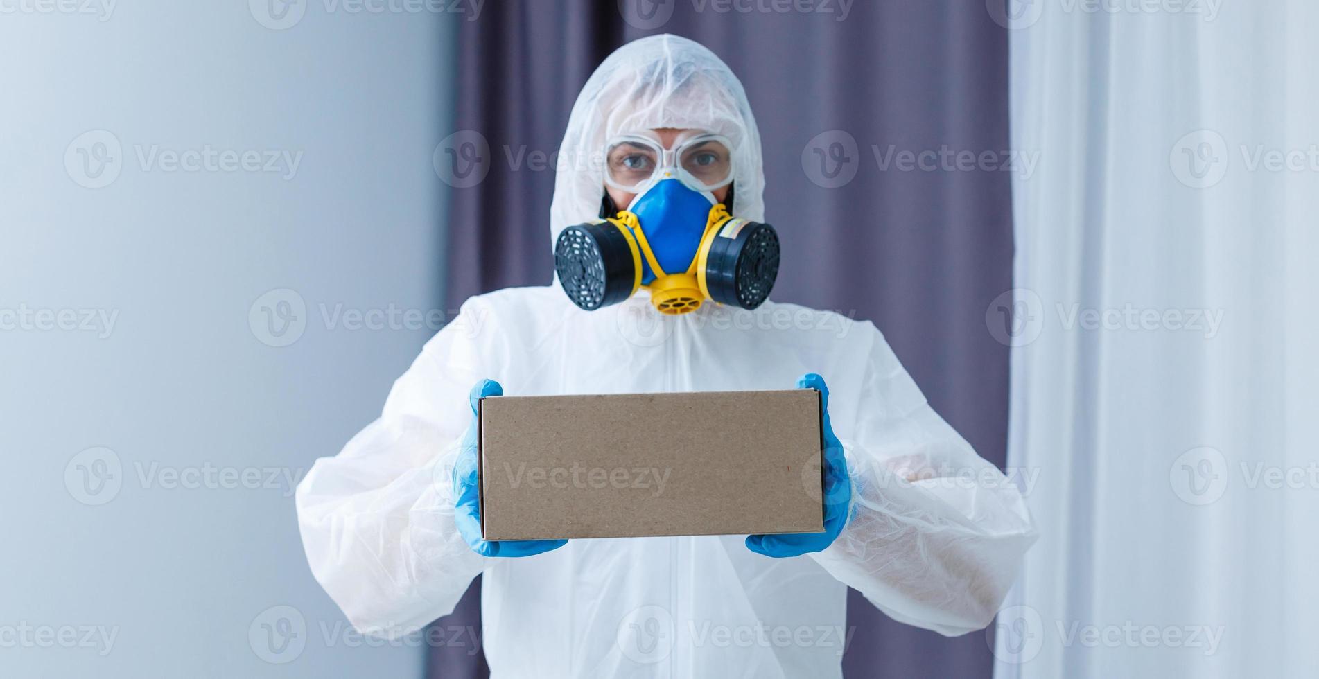 Man in protective suit, a mask and a respirator. Holds a box photo