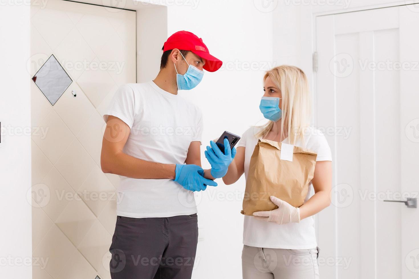 Courier in protective mask delivers parcel, customer in medical gloves receives box. Delivery service under quarantine, disease outbreak, coronavirus covid-19 pandemic conditions. photo