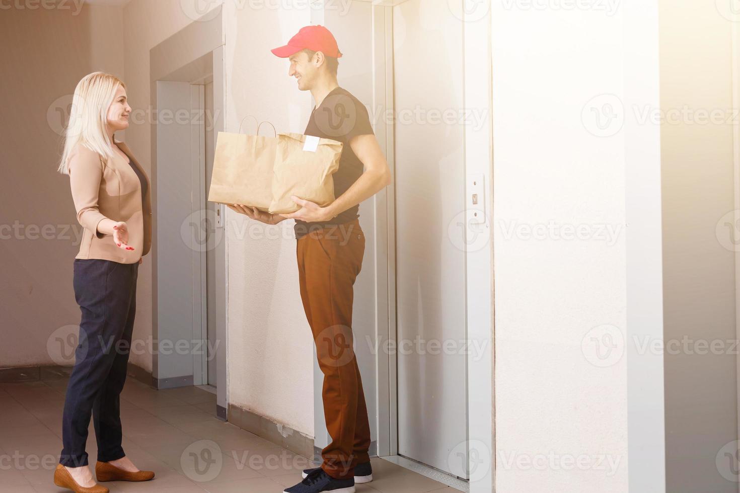 Smiling Young Woman Receiving Groceries From Delivery Man At apartment photo