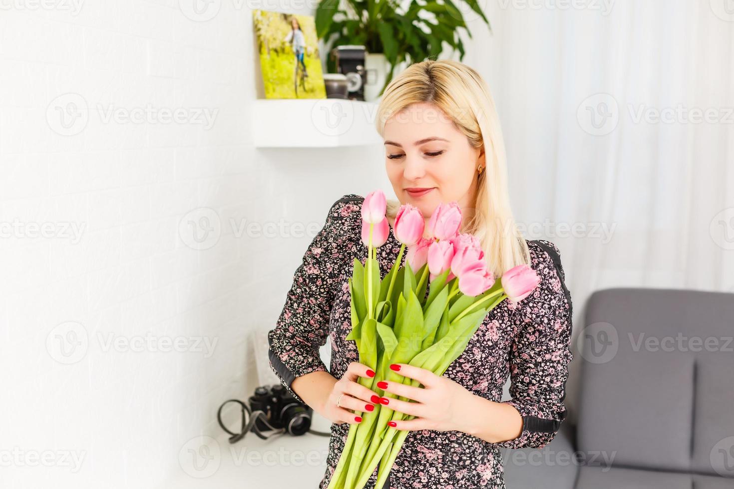 retrato de un hermosa joven niña en vestir participación grande ramo de flores de tulipanes a hogar en el sofá foto