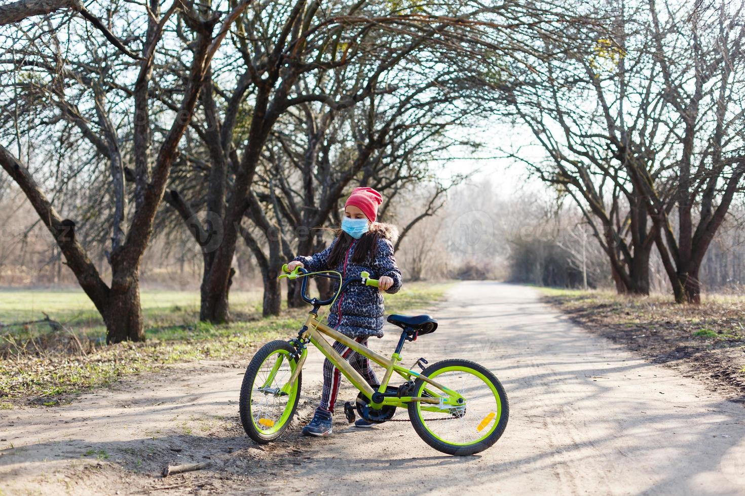 7 years old happy Little girl child ride bicycle in the park at home and wearing protection mask for protect pm2.5 and Coronavirus Covid-19 Pandemic virus symptoms.Sport exercise for health. photo