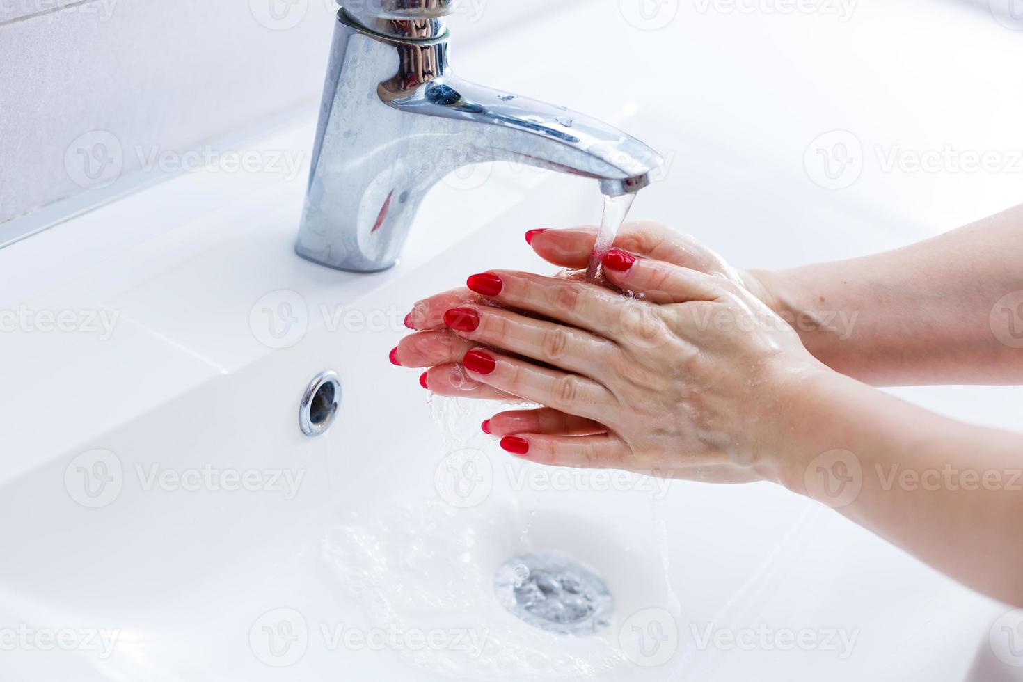 Washing hands in a public restroom focus on the tap, hands in motion photo