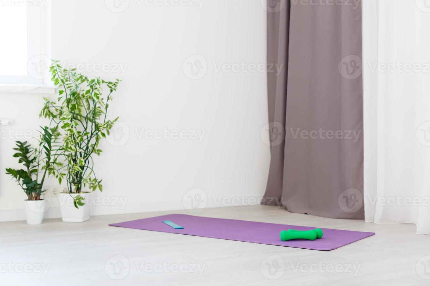 Unrolled yoga mat on wooden floor in modern fitness center or at home with big windows and white brick walls, comfortable space for doing sport exercises, meditating, yoga equipment photo