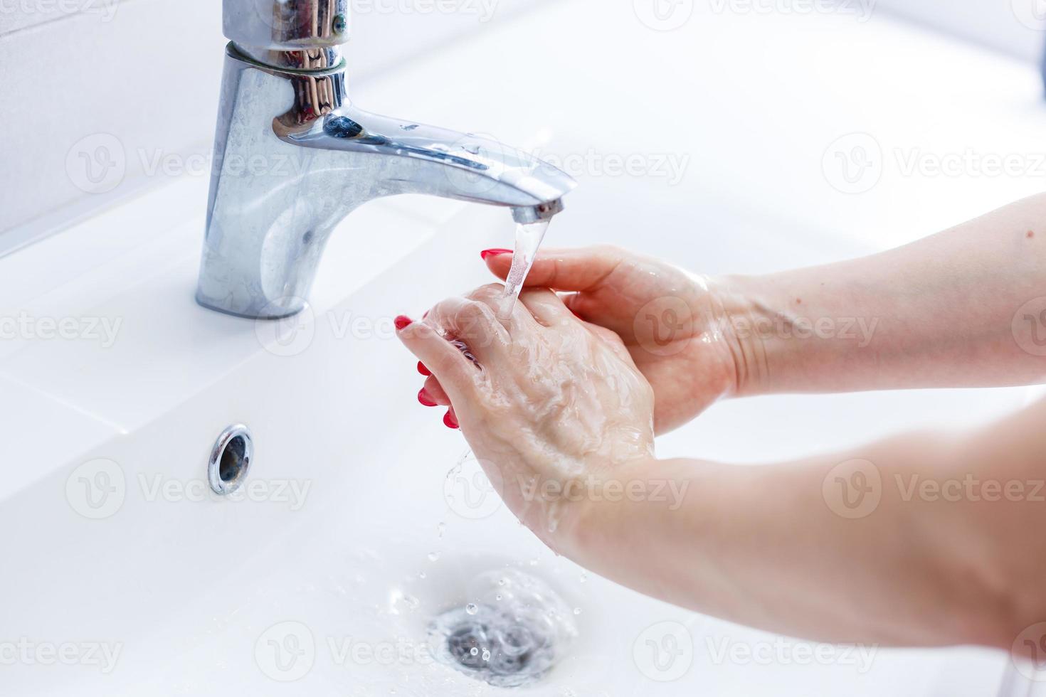 mujer Lavado su manos con jabón debajo corriendo agua desde un inoxidable acero grifo en un blanco cerámico mano cuenca, salud cuidado y higiene concepto foto