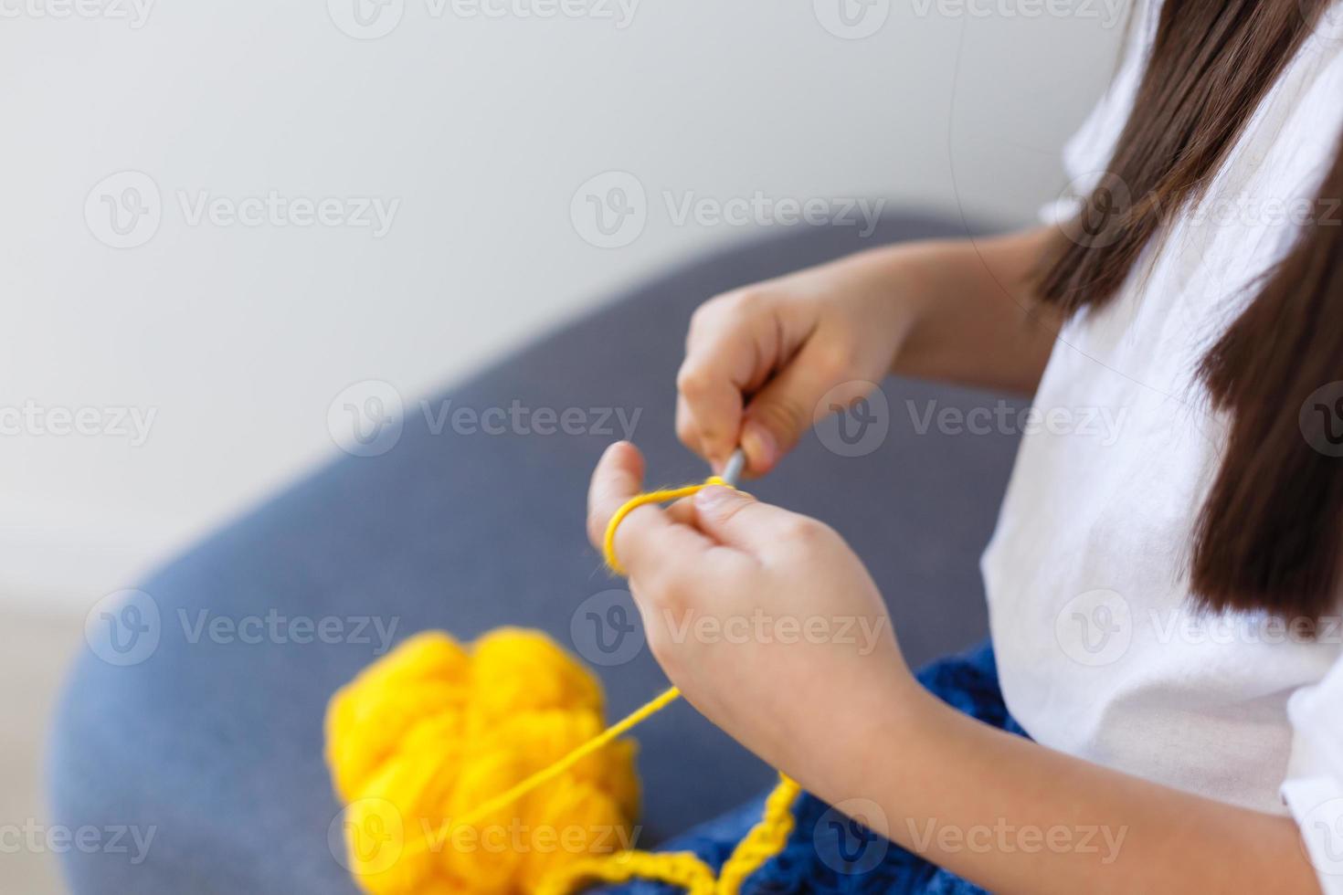 pequeño niña tejer tejer. el niña se sienta en el sofá y tejer desde tejido de punto hilo. tejer grueso hilos. hogar comodidad. foto