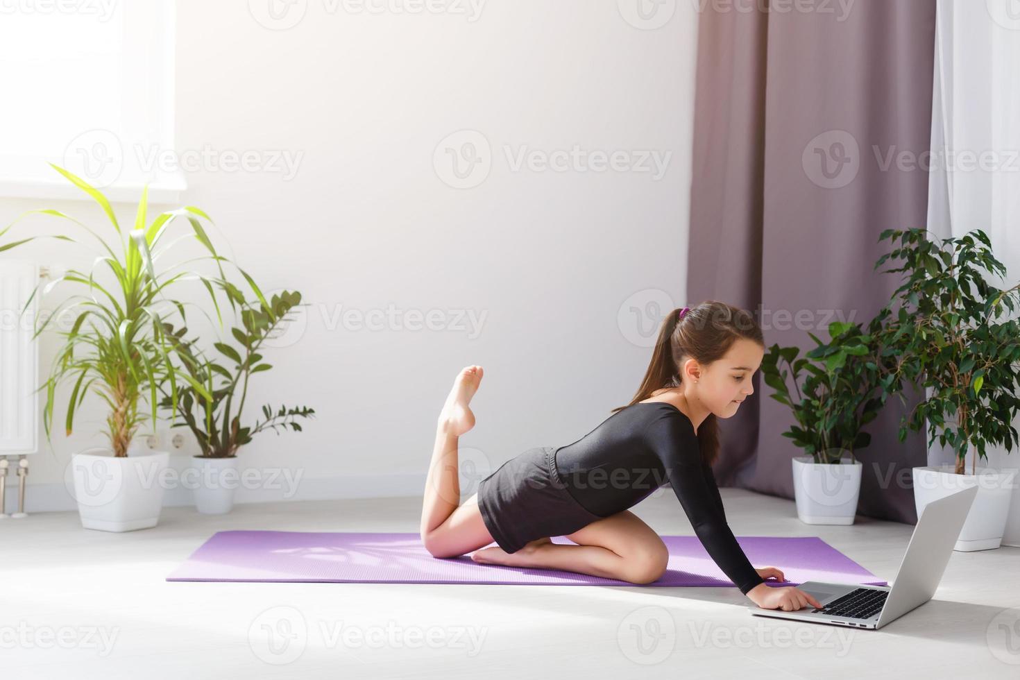 solo niña haciendo yoga ejercicios en línea en ordenador portátil en el piso en el ligero habitación, permanecer hogar seguro mundo. foto