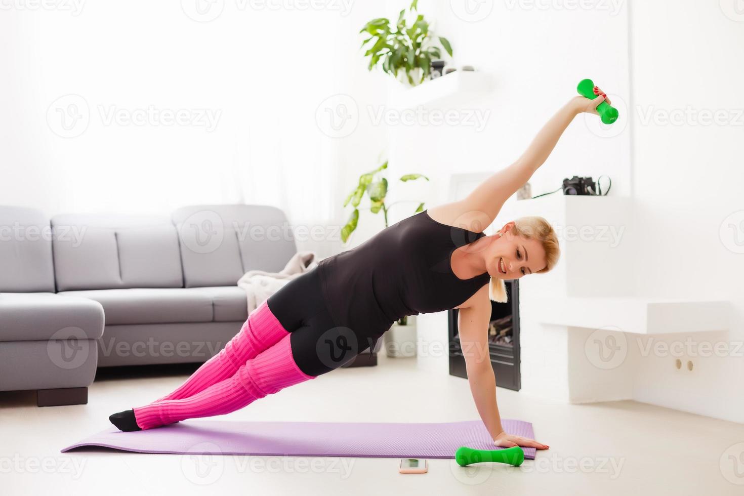 Concept of healthy lifestyle. Close up of young woman hands rolling violet yoga fitness mat before working out at home in living room. Every day morning ritual. Wooden floor, soft light photo