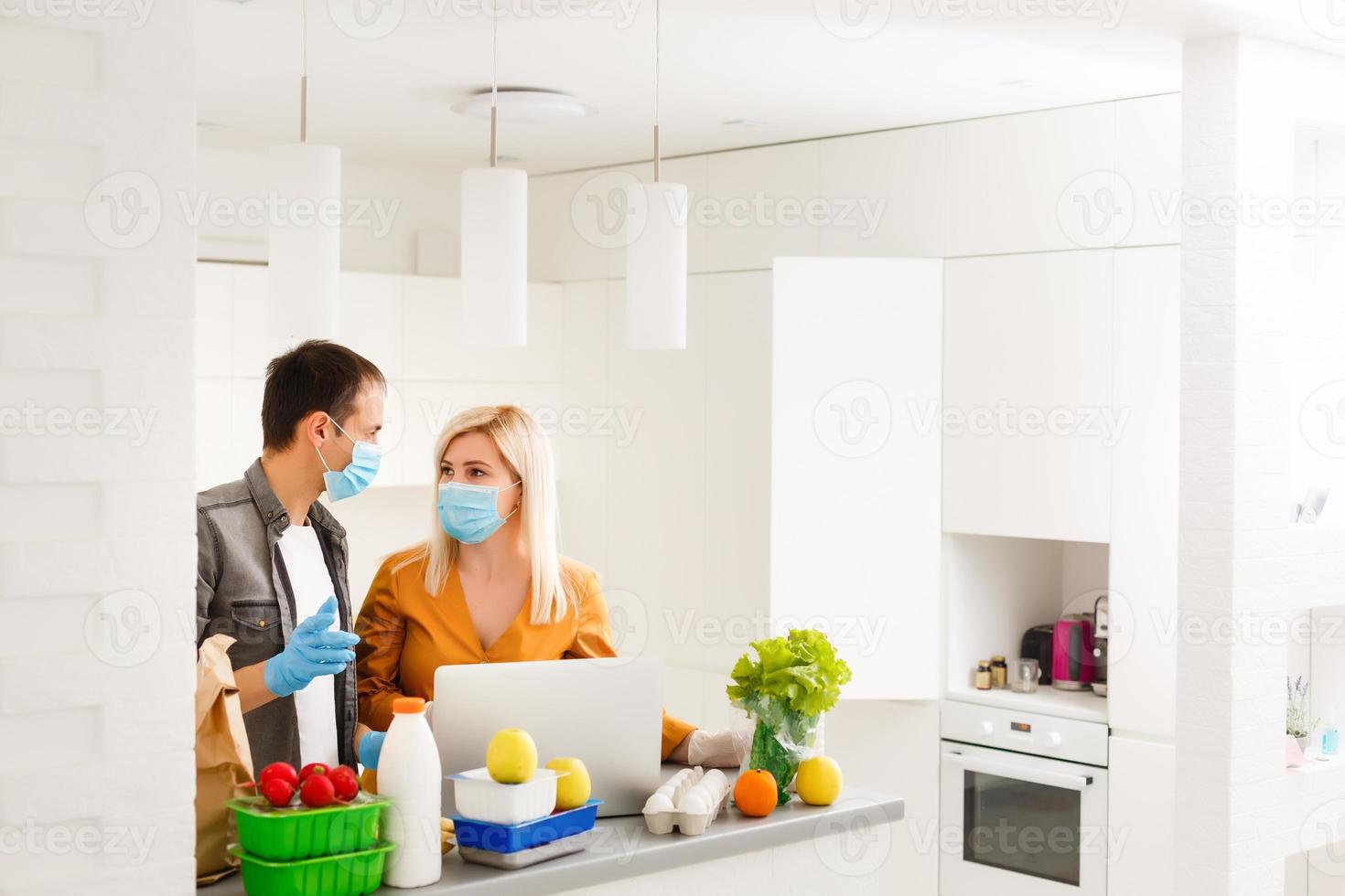 Order food online. Young beautiful couple in kitchen ordering food online from restaurant. Family of two using laptop. Young woman paying with credit card. Nice loft kitchen interior with light bulbs photo