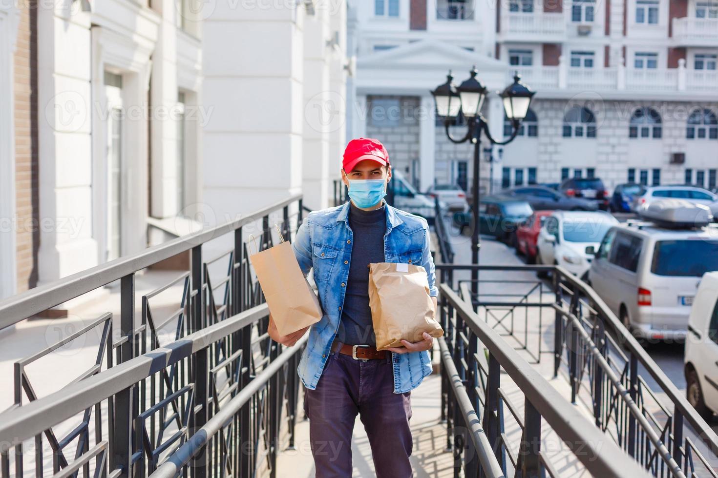 delivery, mail and people concept - man in a protective mask delivering coffee and food in disposable paper bag to customer home photo