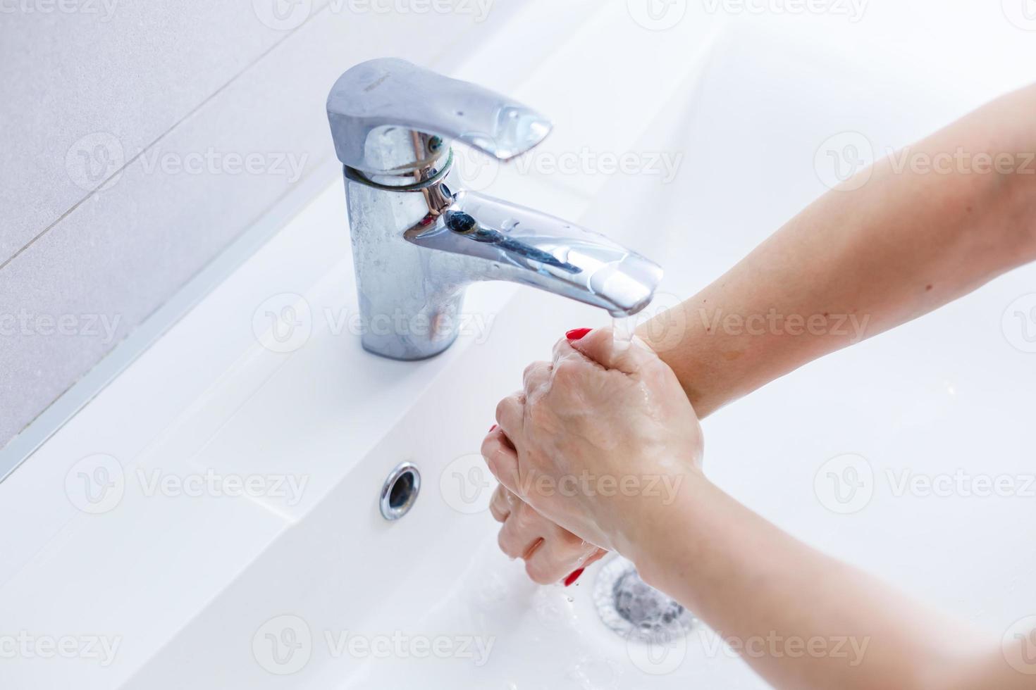 Washing hands in a public restroom focus on the tap, hands in motion photo