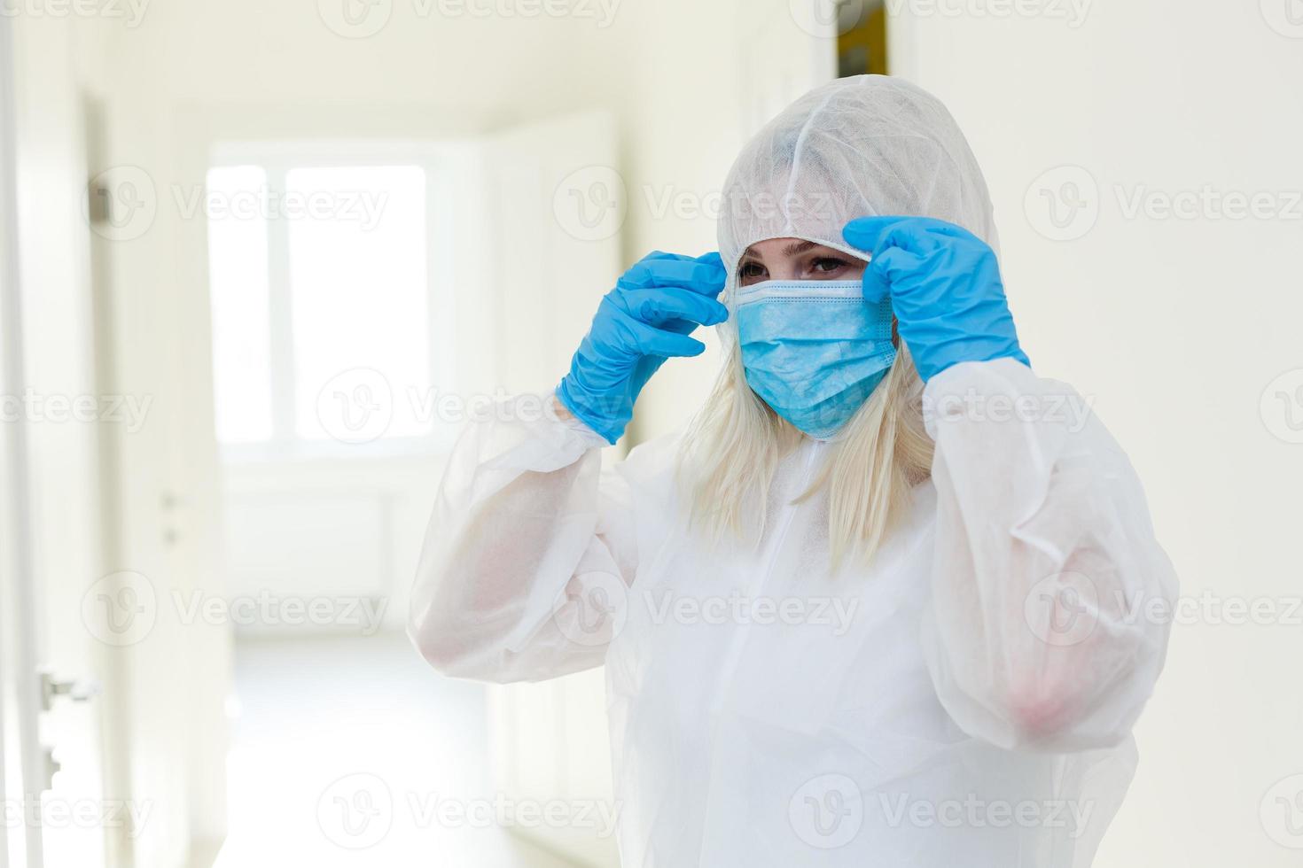 Asian woman puts on a protective mask and suit. Protected against flu, ebola, tuberculosis, virus. Personal protective equipment against biological hazard. photo