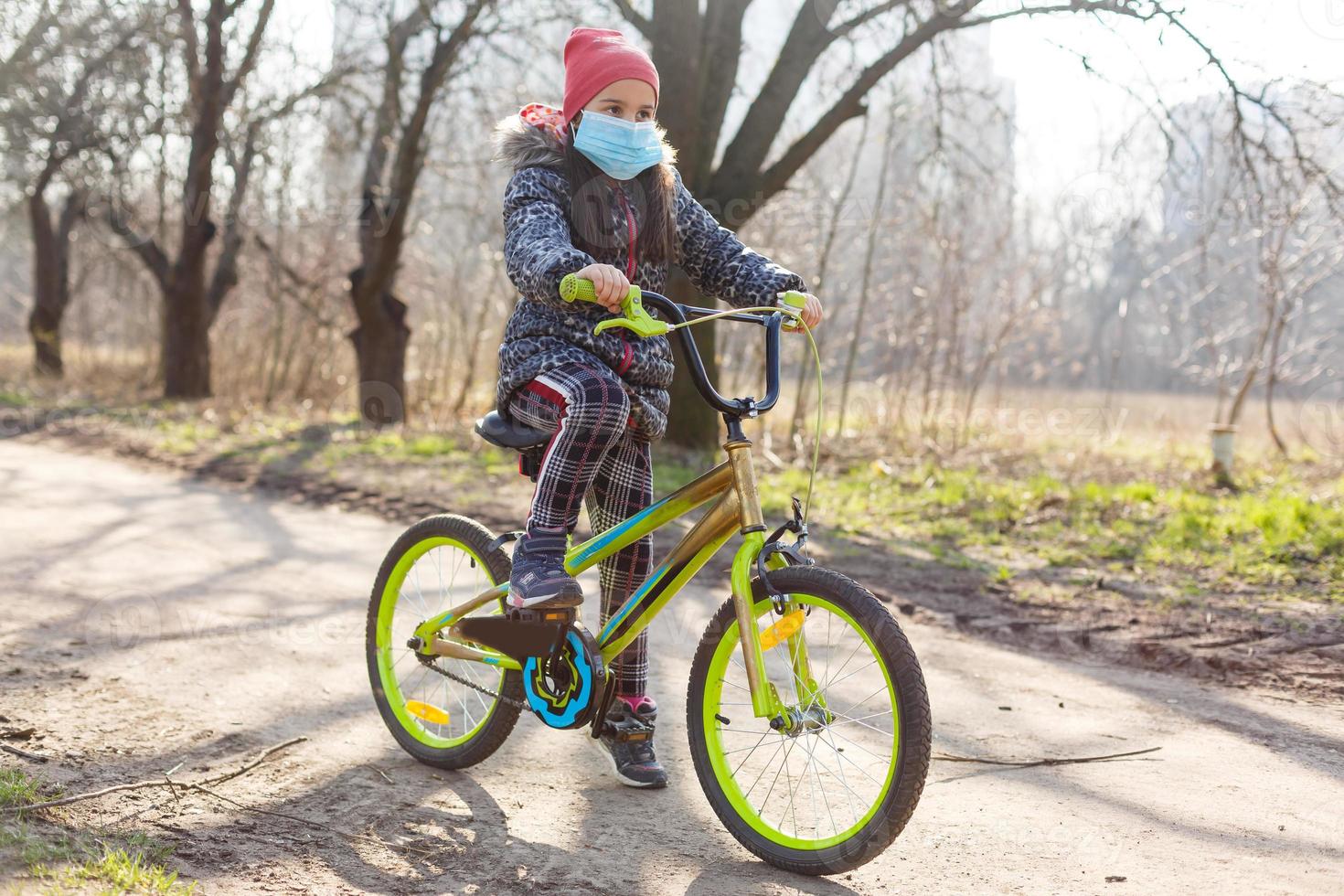 Little girl wearing medical mask prevent flu, pollutions and covid-19 riding bicycle outdoor. photo