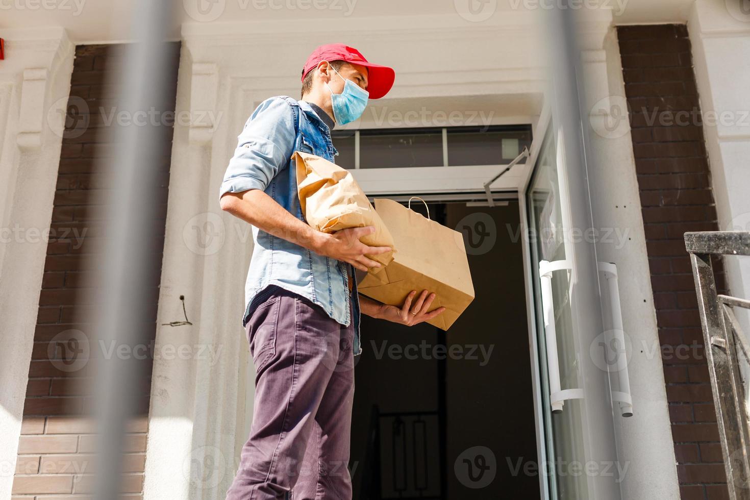 entrega hombre participación papel bolso con comida en blanco Entrada de casa antecedentes , comida entrega hombre en protector máscara foto