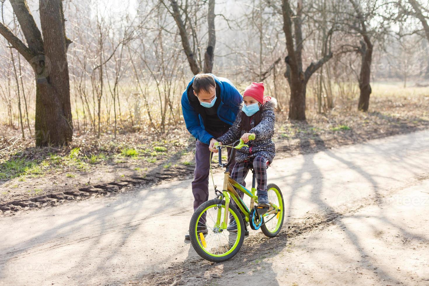 Caucasian father helping daughter ride bicycle wearing protection mask for protect pm2.5 and Coronavirus Covid-19 Pandemic virus symptoms. photo