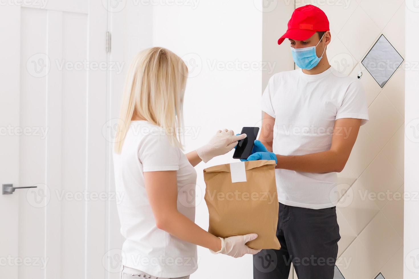 Courier in protective mask delivers parcel, customer in medical gloves receives box. Delivery service under quarantine, disease outbreak, coronavirus covid-19 pandemic conditions. photo