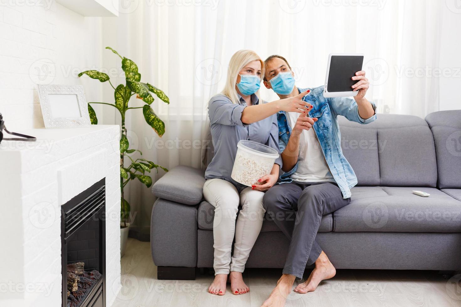 Family couple in medical face masks lying on a bed with a laptop. Concept of watching video, working together and quarantine during a COVID-19 coronavirus epidemic photo