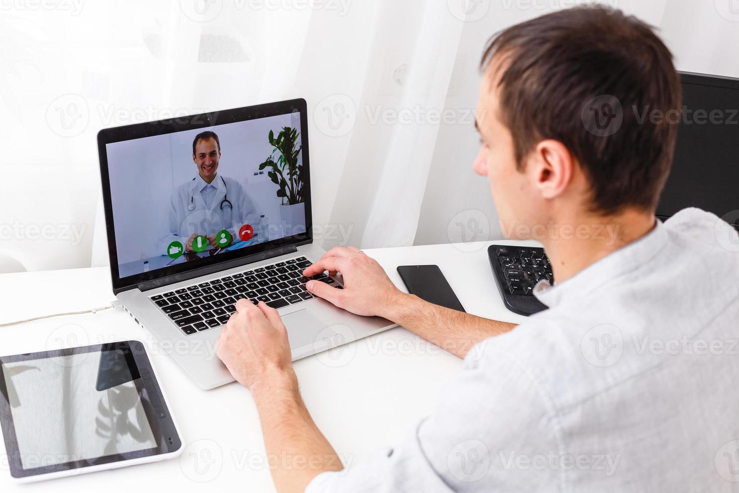 hombre teniendo vídeo charla con médico en ordenador portátil a hogar foto