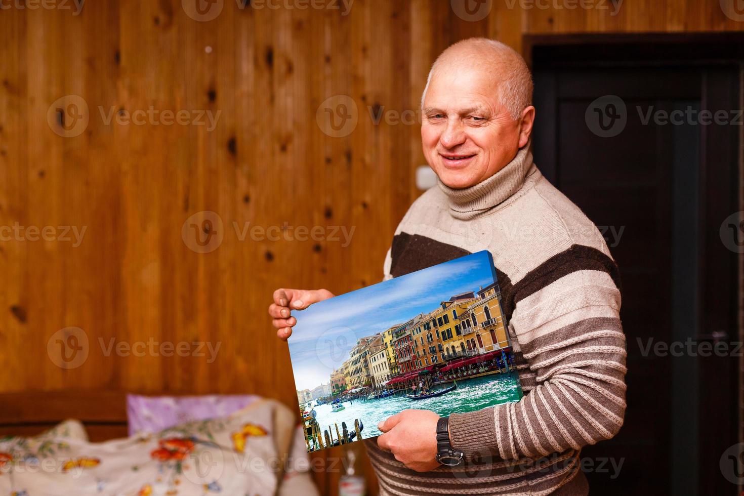 elderly man holding a photo canvas in a wooden house