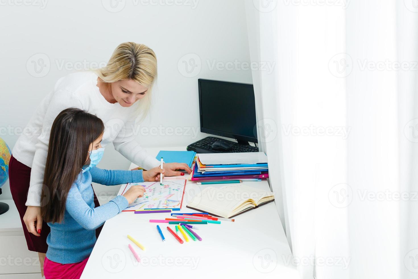 A small girl with her mother are making exercises in copybook at distance home schooling, quarantine photo